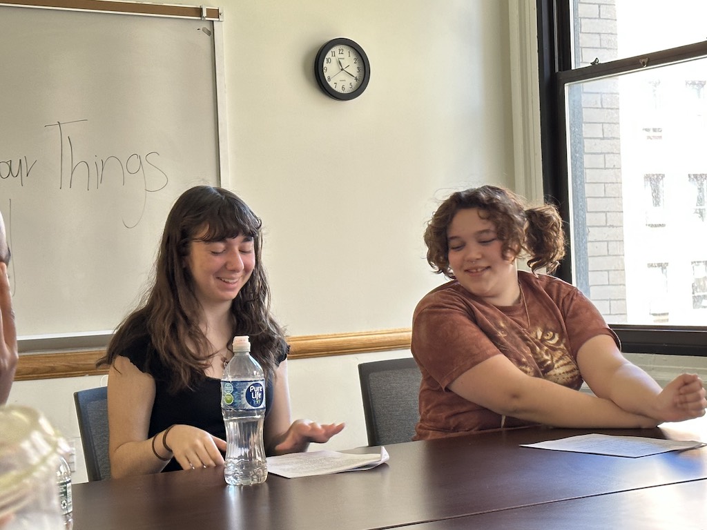 Two Future Dramatic Writers students look down at their scripts, smiling, during class